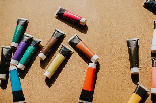 Various coloured paints in tubes, scattered on a table. Space for copy.