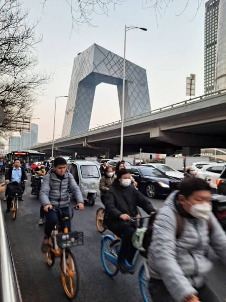 ludzie jeżdżą na rowerach wzdłuż drogi guagnhua we wschodniej 3. pierścieni miasta po pracy wieczorem, na tle chińskiej centralnej wieży telewizyjnej. - beijing traffic land vehicle city street zdjęcia i obrazy z banku zdjęć