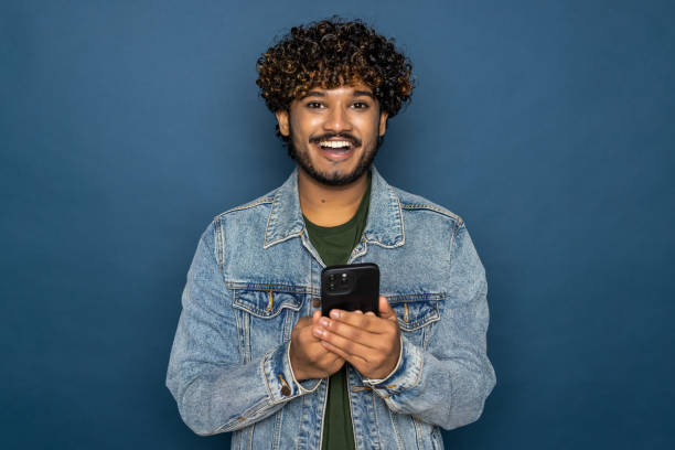 istock Young handsome Indian man using mobile phone on blue background 1475523441
