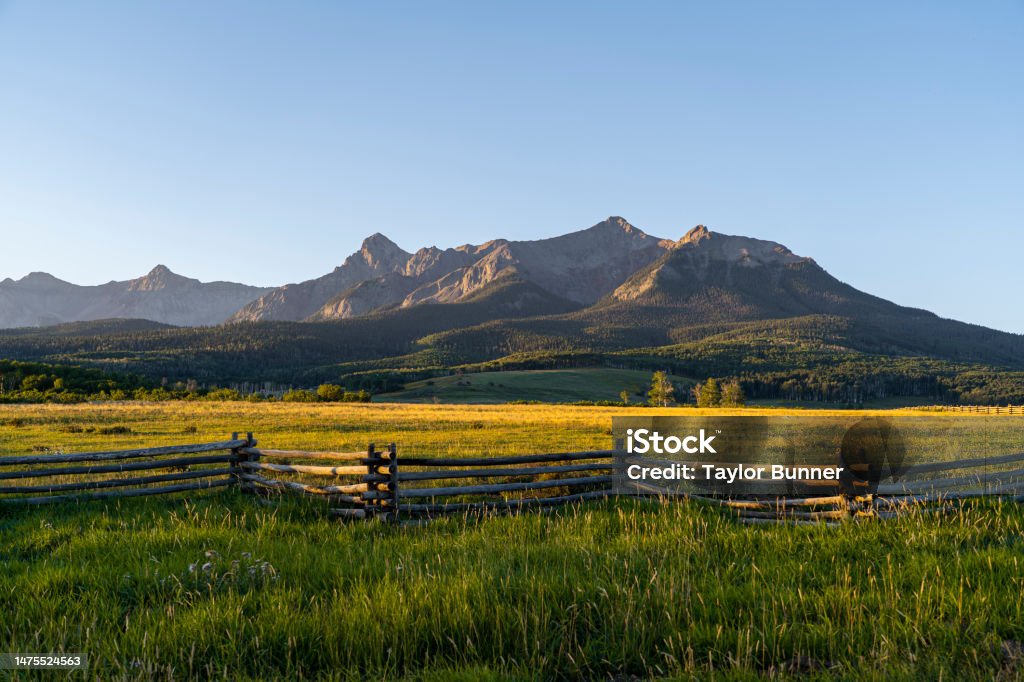 Early morning sunrise at the foot of the mountains in Colorado An early morning sunrise in the San Juan Mountains in southwestern Colorado. Sunlight falls on the landscape below, creating long shadows and contrast in the scene. Not a cloud in the sky. Colorado Stock Photo