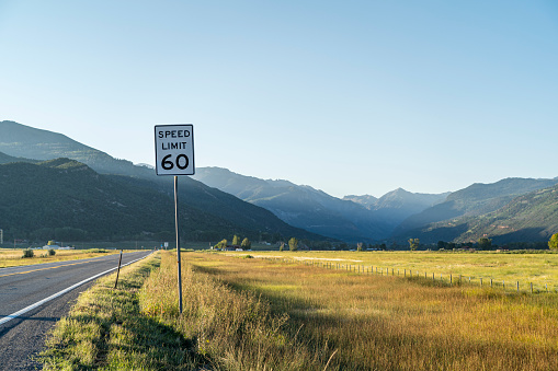 The view from the side of the road in Ridgway, Colorado. Golden hay field on the right, with a paved highway and a speed limit 60 sign on the left, with the San Juan Mountains visible in the distance.
