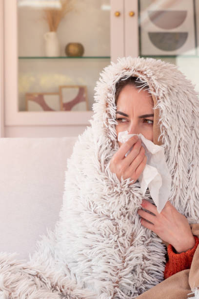 istock Ill woman with high temperature blowing running nose with paper tissue while resting under warm blanket 1475527087