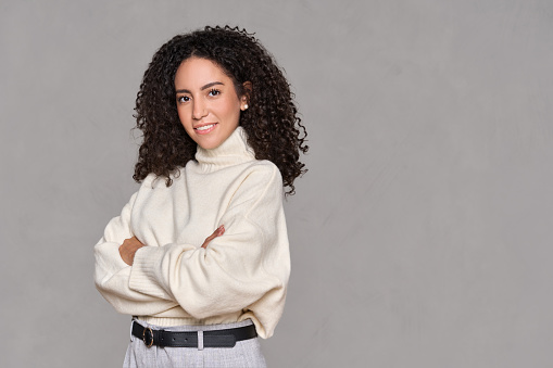 Young adult smiling latin professional business woman, happy hispanic female model manager standing looking at camera arms crossed isolated on light brown background, portrait.