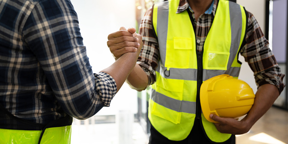 Construction engineer and architect with blueprint shaking hands while standing on construction site. Home building concept.