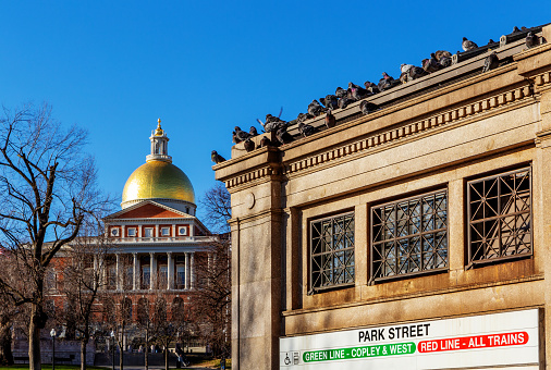 Boston, Massachusetts, USA - March 20, 2023: Close-up of the Massachusetts Bay Transportation Authority's (MBTA) Park Street subway station on the corner of Park and Tremont Streets in downtown Boston. Pigeons on the roof edge. Massachusetts State House in the background.