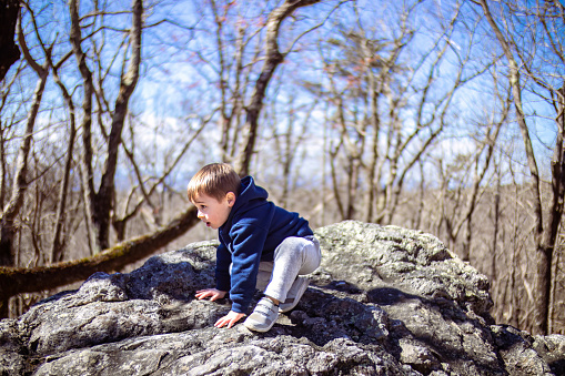Male child enjoying time outside while playing on large natural boulders at Alabama State Park with clear blue sky and forest in background