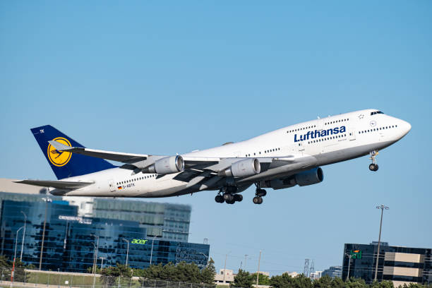 avión comercial de lufthansa despegando de la pista y escalando frente a edificios con el escape de calor del motor foto de archivo. - vapor trail boeing 747 airplane sky fotografías e imágenes de stock