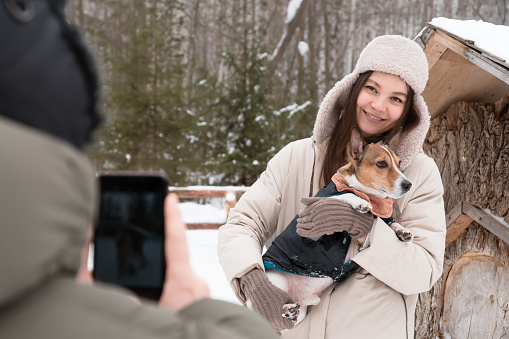 man takes picture of wife with dog using smartphone walking in winter park