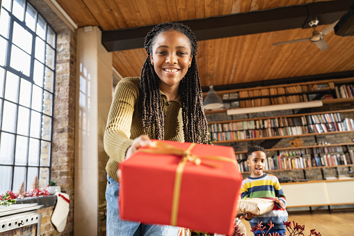 Focus on smiling face of 12 year old Black girl with long locs, wearing casual attire, and celebrating Christmas with family. Young brother in background.