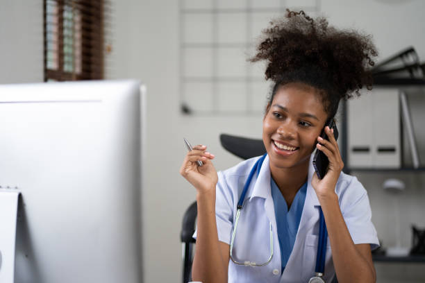 istock Young African american female doctor using smartphone and working with computer while sitting at the clinic room. 1475558903