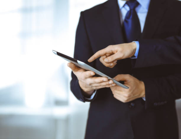 istock Business people use a tablet computer for discussion of their new project, standing in a modern office. Unknown businessman or male entrepreneur with a colleague at workplace 1475559089