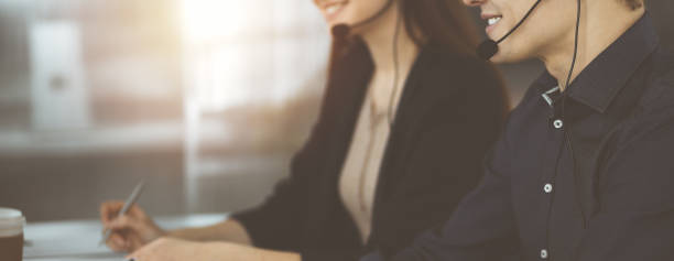 istock Young man with headsets is talking to a client, while sitting in modern sunny office. Call center operators at work 1475559150