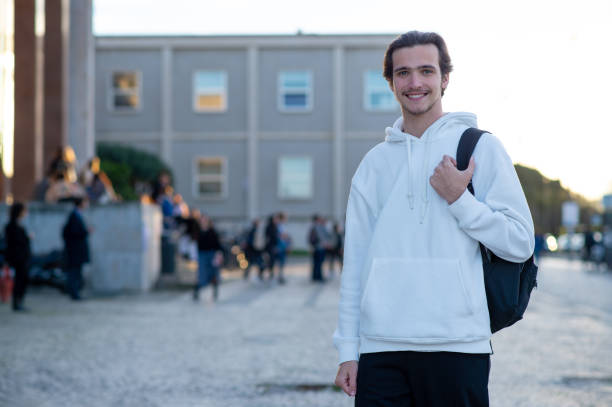 istock Happy young man standing on a sidewalk near his faculty building with a backpack. Student smiling while standing on campus at his university. A cheerful young man with a backpack outdoors. 1475560673