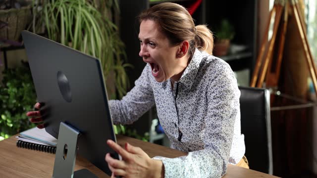 Business woman screaming in shock at computer monitor in office