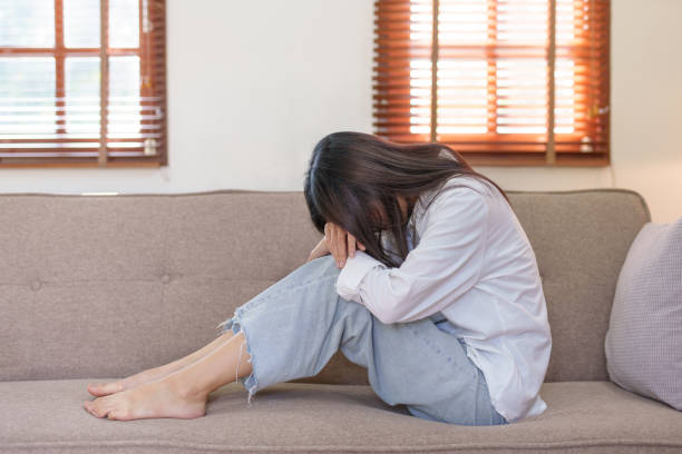 istock Young Asian woman suffering from illness, stress, depression from work sitting alone on sofa at home frustrated. Desperate Asian woman feeling alone. 1475563648
