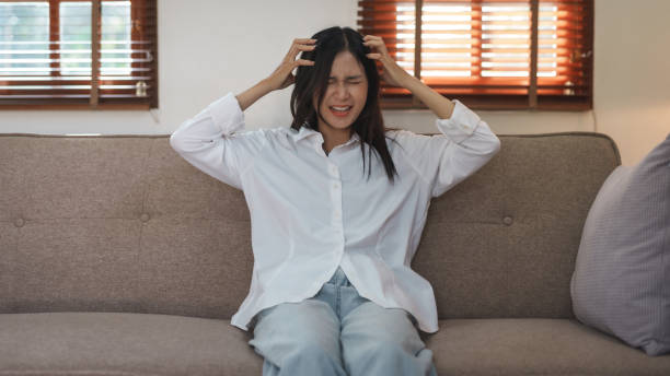 istock Young Asian woman suffering from illness, stress, depression from work sitting alone on sofa at home frustrated. Desperate Asian woman feeling alone. 1475563653