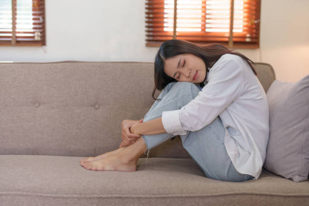 istock Young Asian woman suffering from illness, stress, depression from work sitting alone on sofa at home frustrated. Desperate Asian woman feeling alone. 1475563680