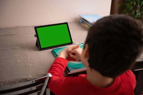 istock Smart student sitting a table a watching online lesson on a digital tablet with empty green chroma key screen copy space 1475565714