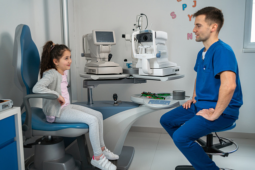 Caucasian little girl talking with an ophthalmologist, at the ophthalmology clinic
