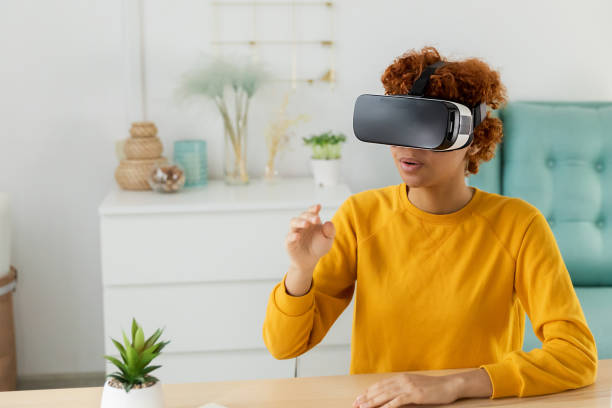 istock African american young woman wearing using virtual reality metaverse VR glasses headset at home. Girl touching air during VR experience on virtual reality helmet. Simulation hi-tech videogame concept. 1475569731