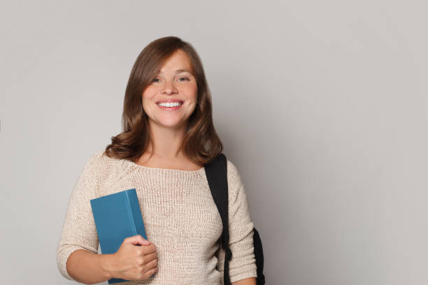 istock Young student woman wearing backpack holding book over isolated grey studio wall background 1475571194
