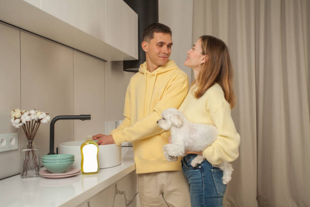 Portrait of  man washing the dishes in the sink and woman holding little white dog in hand, dishwashing liquid with blank label on the table Portrait of  man washing the dishes in the sink and woman holding little white dog in hand, dishwashing liquid with blank label on the table dog dishwasher stock pictures, royalty-free photos & images