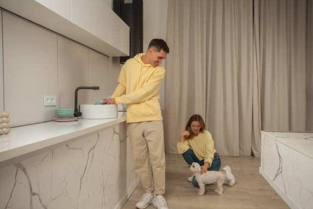 Man washing the dishes in the sink and woman sitting and petting white dog Man washing the dishes in the sink and woman sitting and petting white dog dog dishwasher stock pictures, royalty-free photos & images