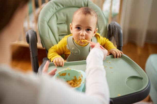 istock Mother spoon feeding her baby son at home 1475572622