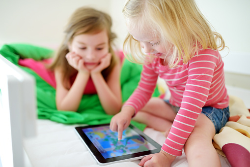 Two little sisters having fun while using digital tablet computer