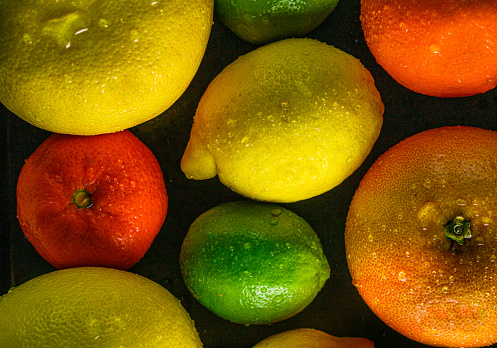 Collection of citrus fruits. A organic tangerine with a leaf and plan stem, a half  mandarin, a half lime and a whole green pomelo oroblanco arranged on a white tablecloth background.