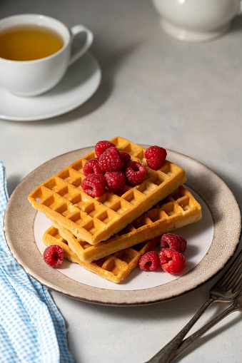 Breakfast waffles with berries in plate served with cup of tea