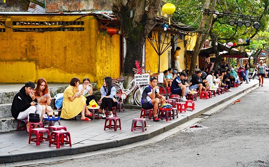 Hoi An, Vietnam - February 22, 2023 - locals enjoy street food at short tables and chairs on a street in Hoi An, Vietnam. Vietnam is well-known for delicious and inexpensive street fare.