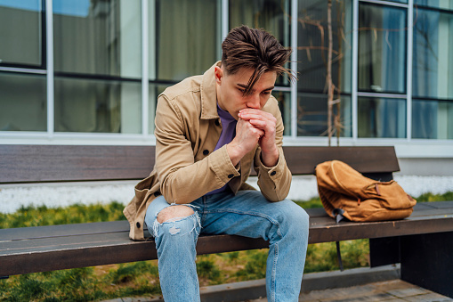 Young man sitting on the bench in the city, looking sad and distraught