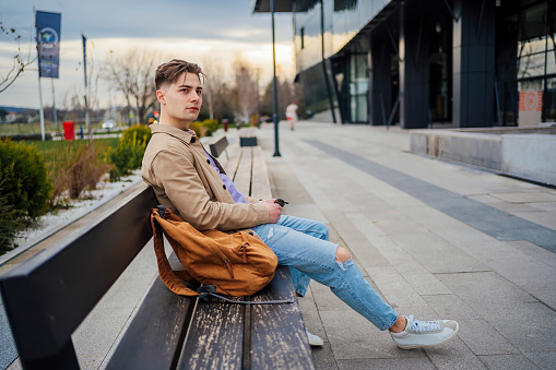 Young pensive man sitting on the bench in the city