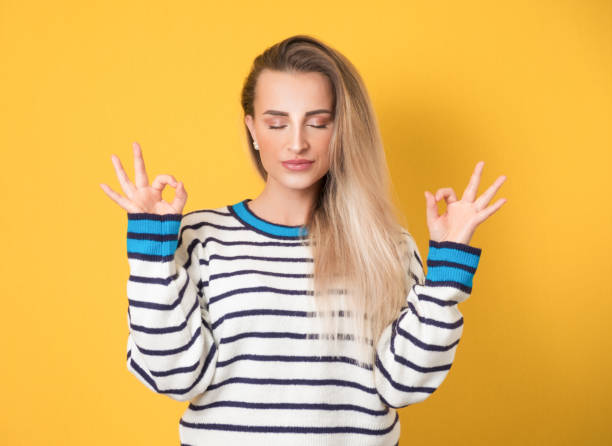 Concentration and enjoying. Young woman with closed eyes shows excellent sign with finger while enjoying, isolated on yellow background. Yes or excellent gesturing, body language concept stock photo