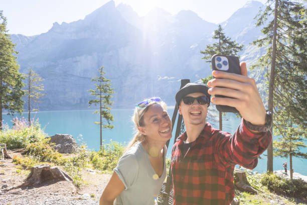 Two people take selfie while hiking around beautiful alpine lake stock photo
