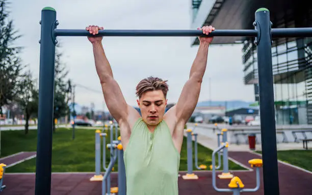Young muscular sporty man exercising in a recreational park, doing pull-ups