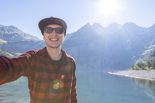 Happy hiker takes photo with the lake and mountains on background.\nPeople travel outdoor activities in Summer