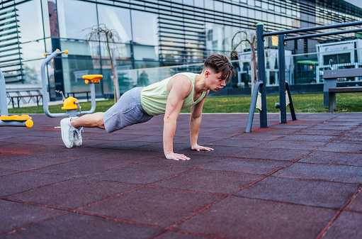 Young handsome muscular man training in an outdoor gym. Doing push-ups