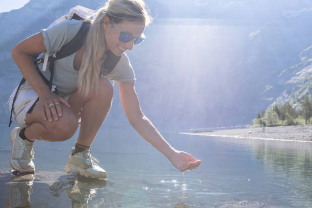 istock Young woman scooping water from a beautiful fresh alpine lake 1475595231
