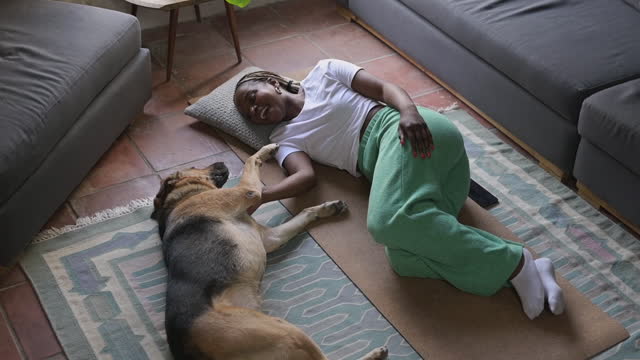 Dog, pet and overhead with a black woman on the living room floor, stroking her canine companion. Happy, smile and bonding with a young female puppy owner petting her german shephard in the home