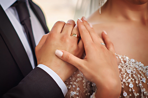 Elegant groom holding bride's hand, posing together outdoors on wedding day.