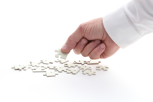 A man's hand holding white puzzle pieces, with part of the sleeve in frame.