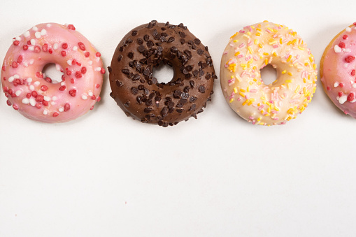 Four donuts in a row - white, pink and chocolate on a white background top view.