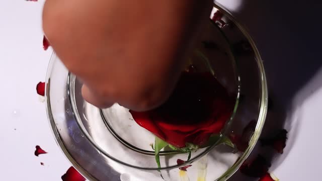 Colorful flowers in a bowl filled with water table top spin view. Human hand taking out the flowers from water for workship.