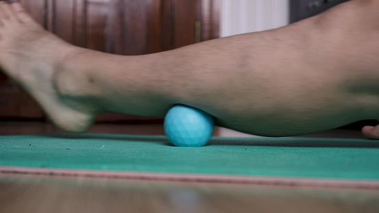 A man does thigh self-massage using a massage ball indoors. Yoga.