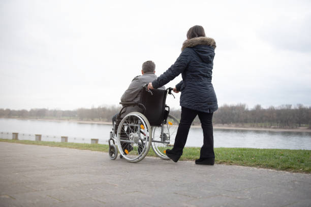 A woman pushes a disabled person in a wheelchair stock photo