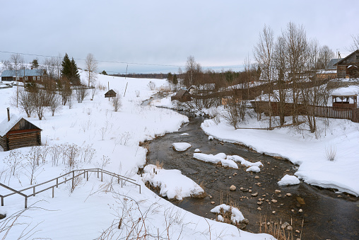 Winter view of the village along the shores of a not frozen small river. Ferapontovo village, Vologda region.
