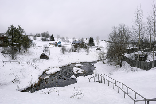 A beautiful landscape with a view of the village located on the snowy banks of a non -frozen river. Ferapontovo village, Vologda region.
