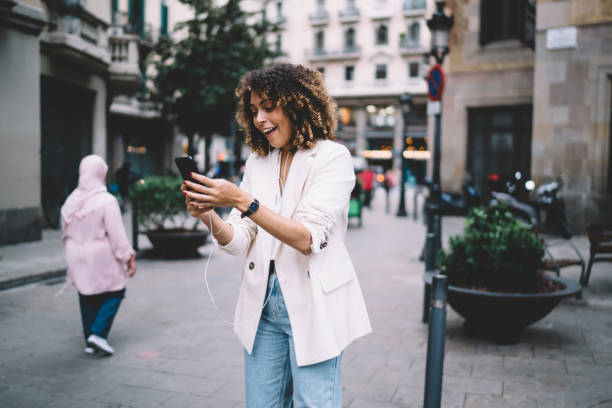 istock Surprised woman reading funny web publication during city sightseeing using smartphone gadget and electronic headphones for listening audio excursion, happy tourist in earphones browsing networks 1475615761